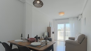 A dining area with a table set for four, a sofa, and a balcony with a view. - 099 - Parque y playa 007 - comfortHOLIDAYS (Santa Pola)