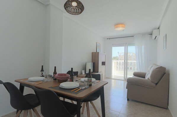 Un área de comedor con una mesa dispuesta para cuatro personas, un sofá y un balcón con vistas.