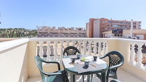 A balcony with a table set for two, chairs, and a view of buildings in the background. - 099 - Parque y playa 007 - comfortHOLIDAYS (Santa Pola)