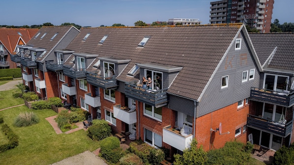 Eine Reihe moderner Apartmentgebäude mit mehreren Balkonen, einem gepflegten Garten und blauem Himmel.