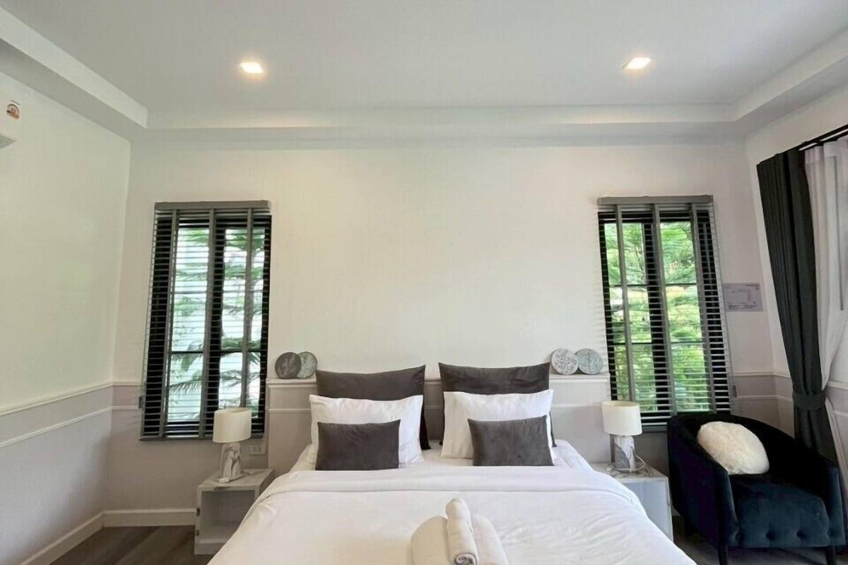 A hotel room with a large bed, two bedside tables with lamps, a chair, and two windows with shutters.