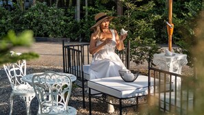 A woman sitting at a table under a white umbrella in a garden setting with metal chairs and a decorative fountain. - Tarn Villa Krabi (Krabi)