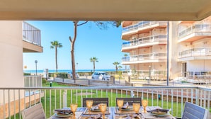 Een balkon met eettafels, met uitzicht op een strand en een parkeerplaats.