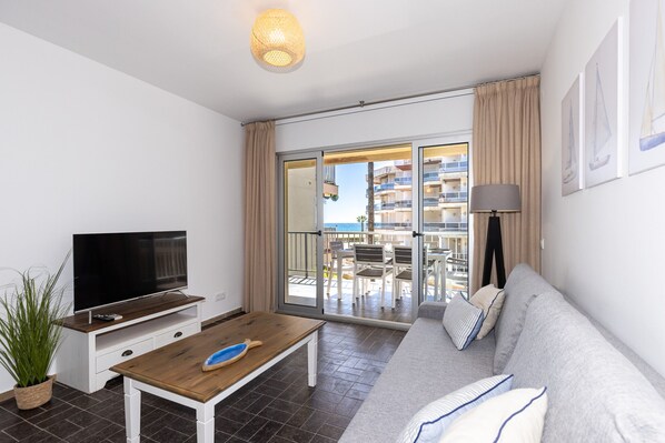 Un salon moderne doté d’un téléviseur à écran plat, d’une table basse en bois, d’un canapé gris et d  ’un balcon aménagé avec du mobilier d’extérieur.