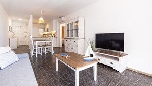 A modern living room with a sofa, a dining table, a TV, and a kitchen in the background.