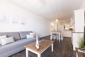 Un salon moderne avec un canapé gris, une table basse en bois et une maquette de voilier.