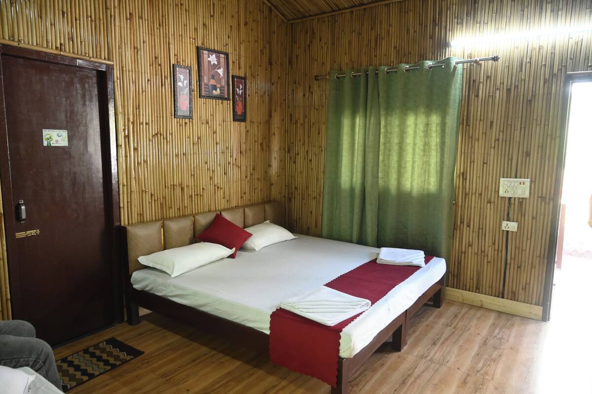 Una habitación con pared de madera, cama con ropa de cama blanca y roja, cortina verde y una puerta con cerradura.