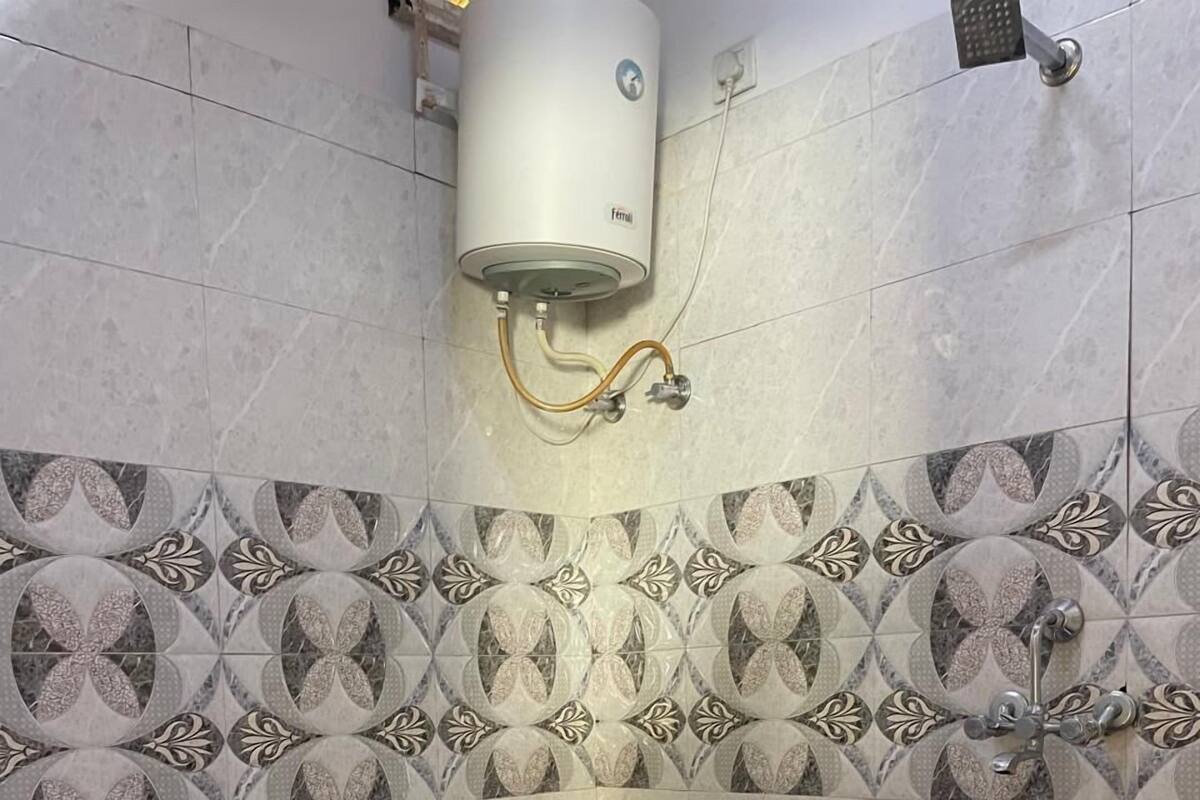 Un baño con inodoro, ducha y calentador mural, además de un salpicadero decorativo de azulejos.