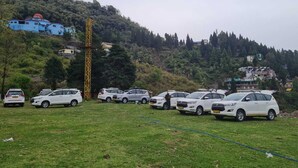A parking area with several white SUVs parked on a grassy field, surrounded by a hillside with buildings and trees. - Ivory Estate Kyarkuli (Dehradun)
