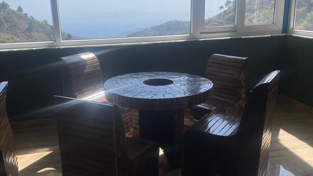 A room with a round wooden table and chairs, large windows with a view of a mountainous landscape. - Ivory Estate Kyarkuli (Dehradun)