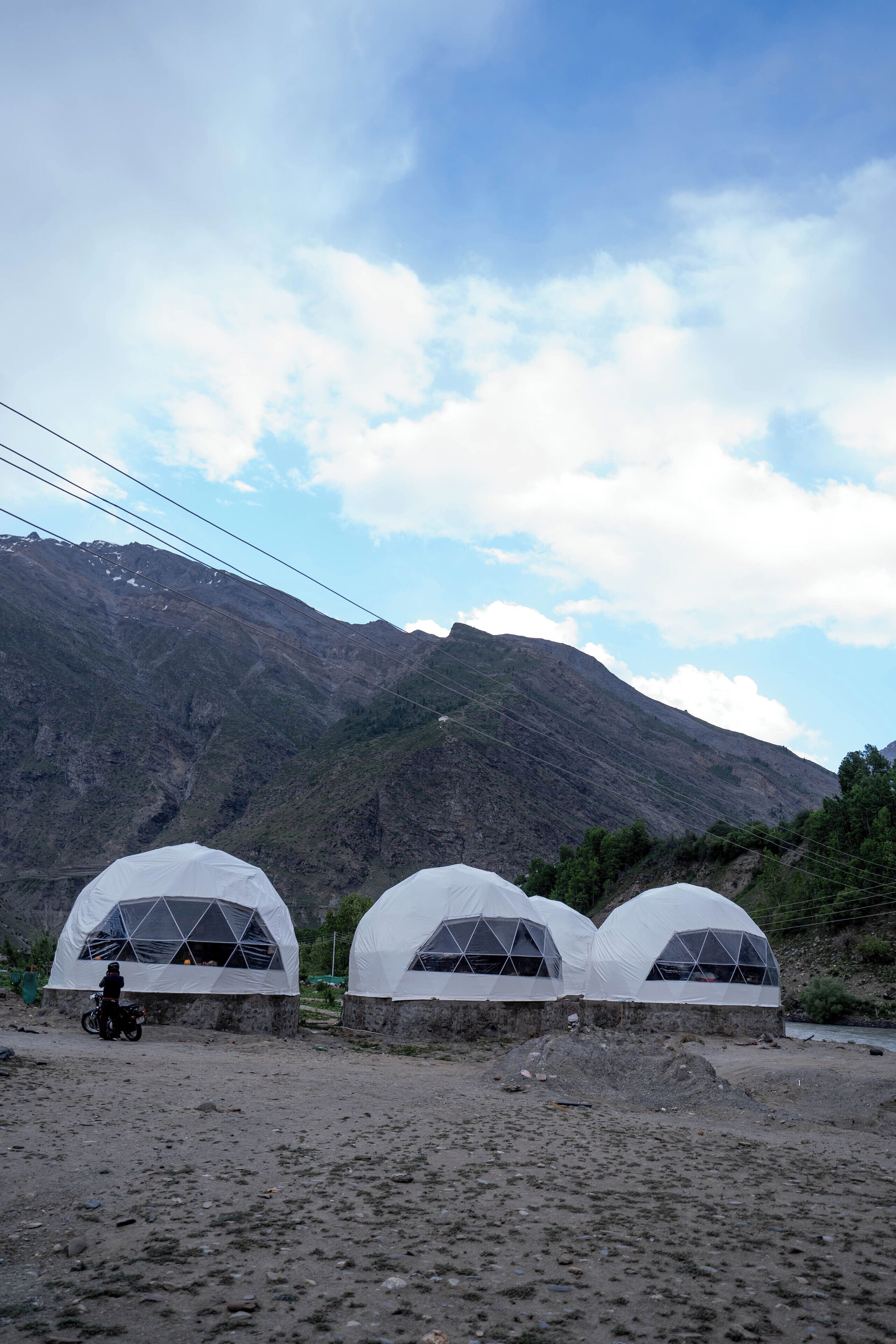 Three dome-shaped tents with a person riding a motorcycle in front.