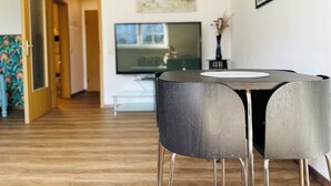 A modern living room with a round table and two chairs, a flat-screen TV, and a painting on the wall. - Pet-friendly one-room vacation apartment at the spa gardens (Bad Rodach)