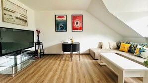 A modern living room with a flat-screen TV, a round table, and a sofa with floral cushions. - Pet-friendly one-room vacation apartment at the spa gardens (Bad Rodach)