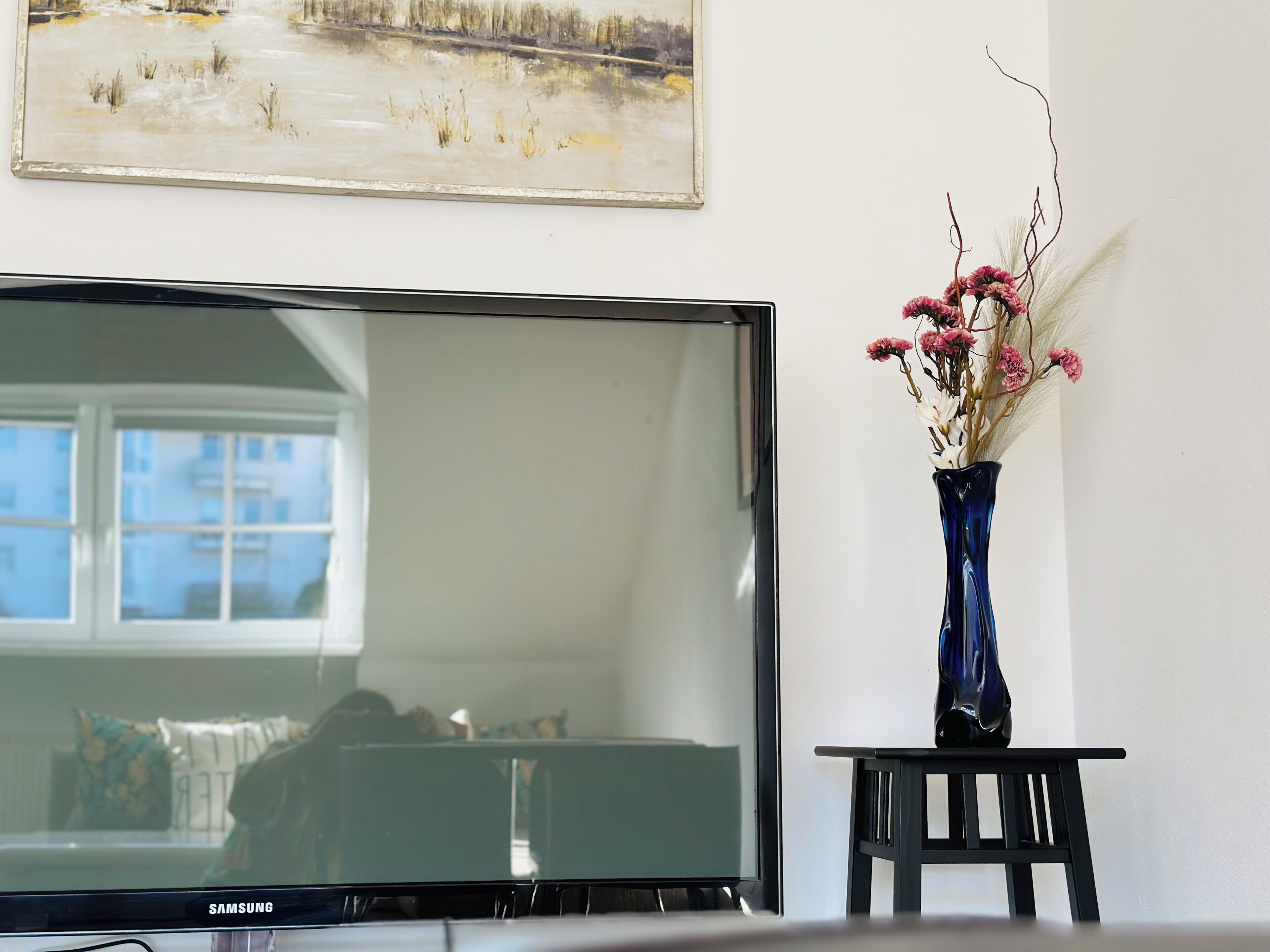A television on a stand, a vase with flowers, and a painting on the wall.