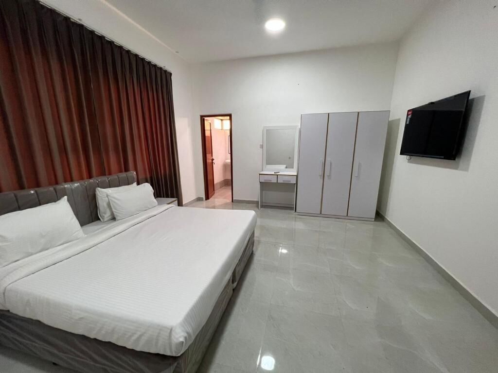Ein Schlafzimmer mit Bett, Kleiderschrank, Spiegel, Fernseher und einem Badezimmer mit Waschbecken.