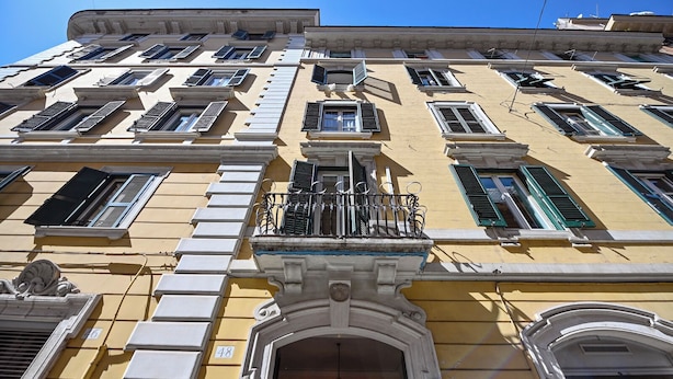 A multi-story building with a yellow facade, multiple windows with shutters, and a central balcony with a wrought iron railing. - Imperium penthouse with terrace (Roma)