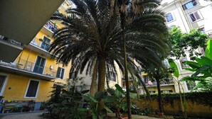 A courtyard with a palm tree, potted plants, and a yellow building with balconies. - Imperium penthouse with terrace (Roma)