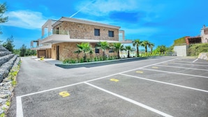 A modern two-story building with a stone facade, a balcony, and a parking lot with marked spaces. - Epta Villas Luxury Redefined (Kassandra)