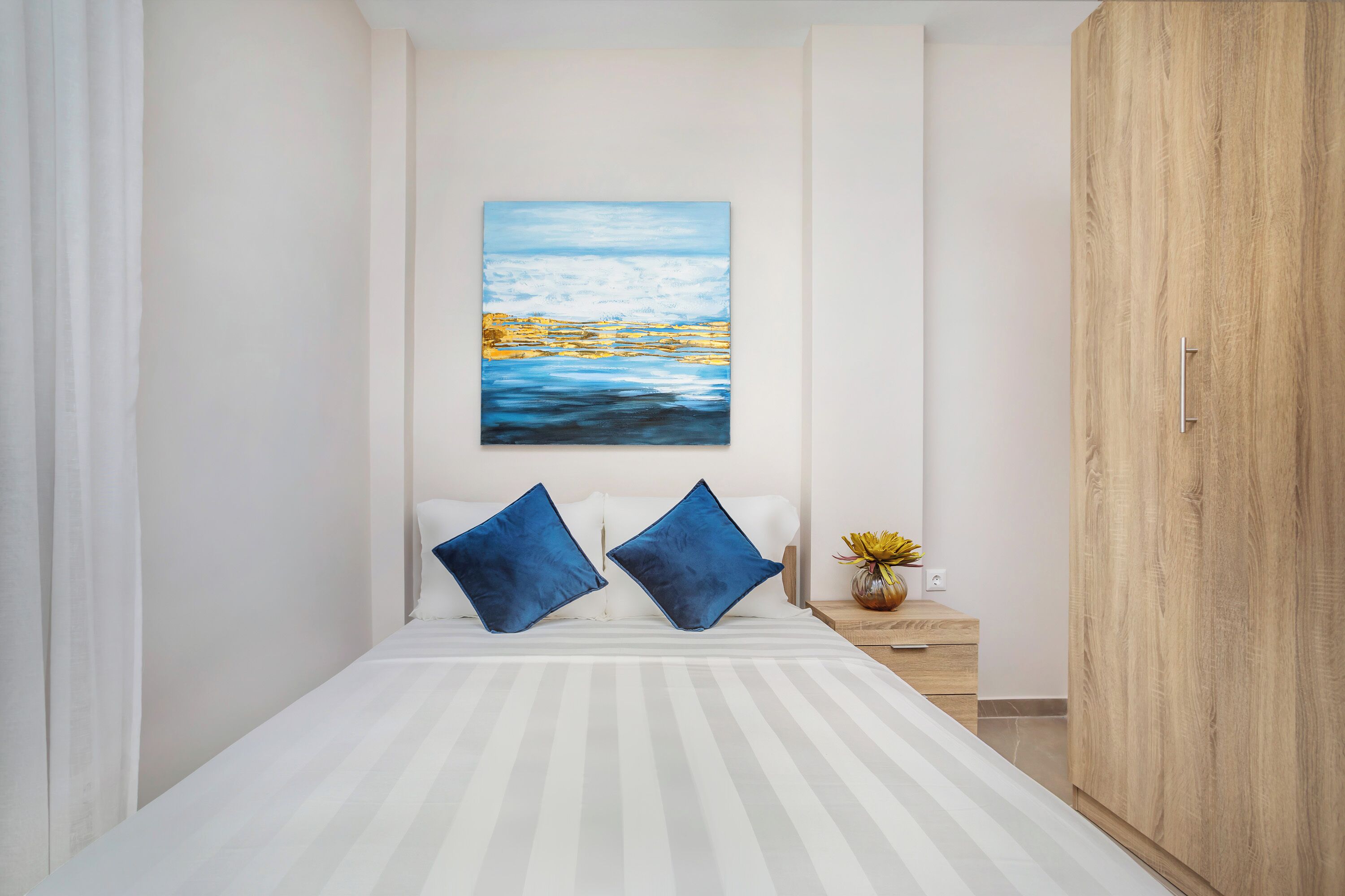 Ein Schlafzimmer mit einem Bett, zwei Kissen, einem Nachttisch mit einer Vase und einem Gemälde an der Wand.