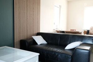 A modern living room with a black leather sofa, a glass coffee table, and a wooden slatted wall. - Time out in Märkische Schweiz (Müncheberg)