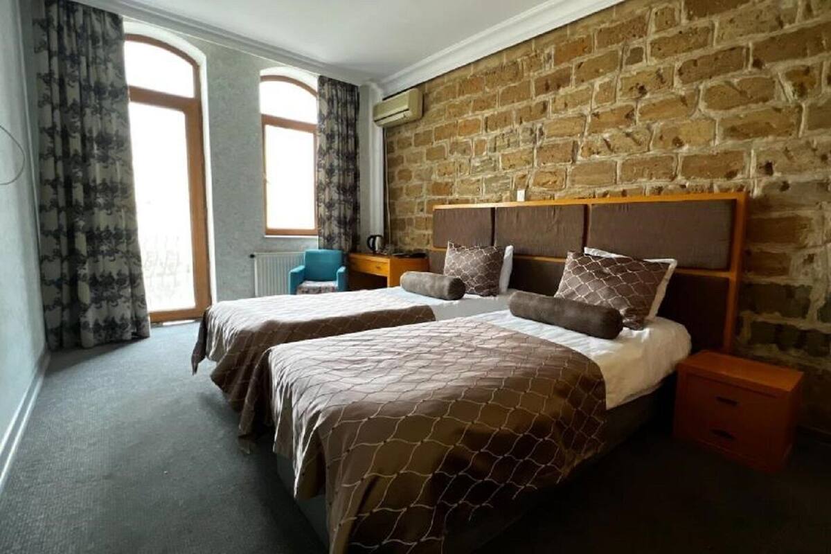 A bedroom with two beds, a brick wall, a window, and a nightstand.