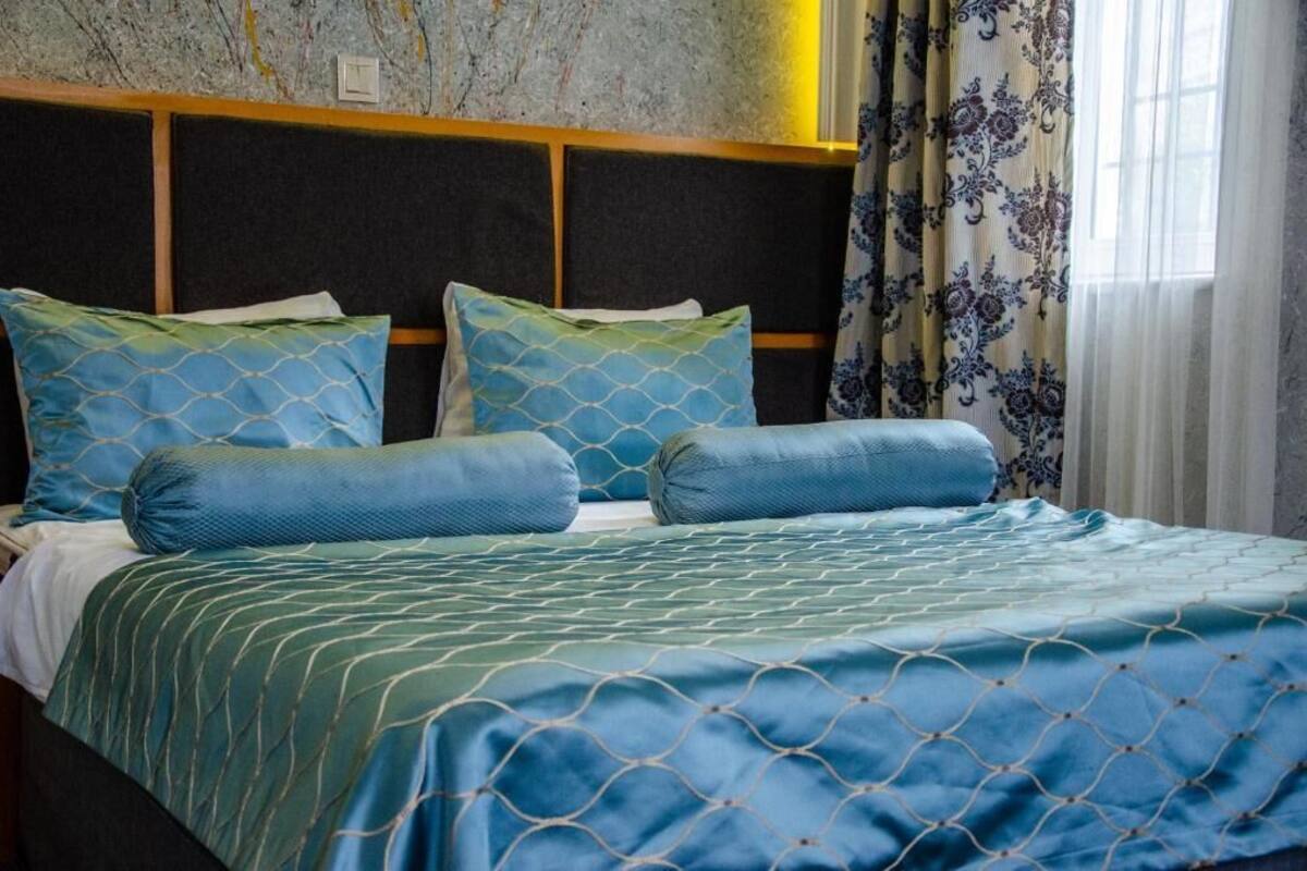 A hotel room with a bed featuring a blue and green patterned bedspread, matching pillows, and a headboard with a wooden panel design.