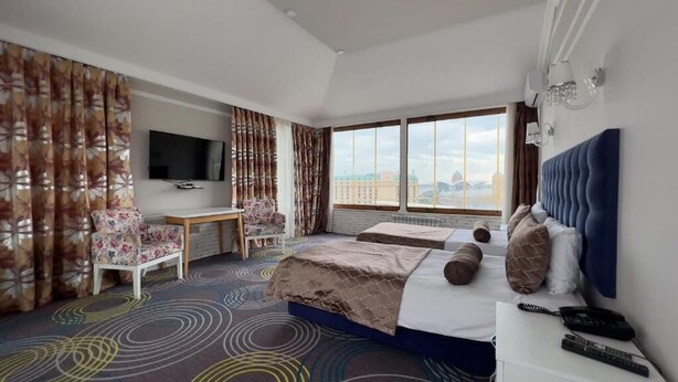 A hotel room with a bed, a desk, a TV, and a large window with a view. - Senator Boutique Hotel Baku (Baku)