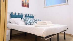 A neatly made bed with white linens and teal pillows, a window with a view, and a painting on the wall. - Visit Rome from a quiet place Frascati (Frascati)