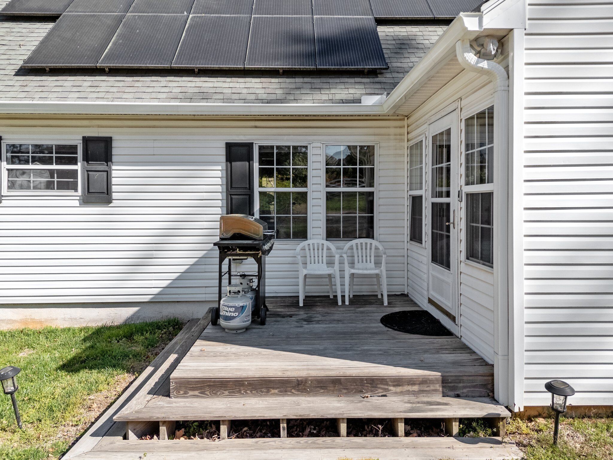 A house with a covered porch, a grill, and two white plastic chairs.