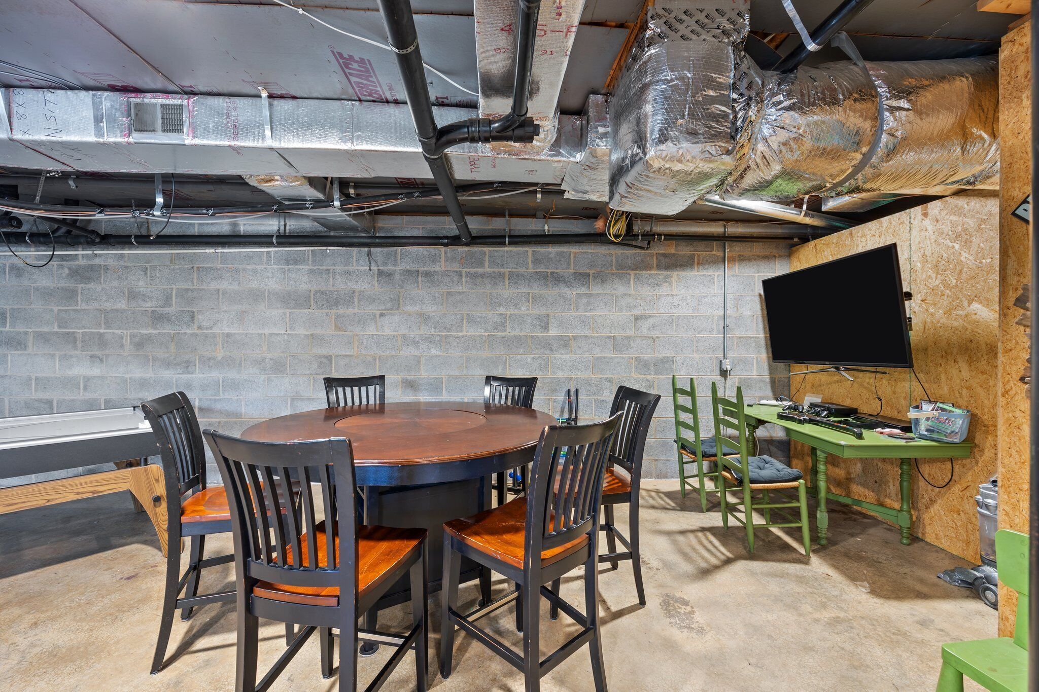 A conference room with a round table, six chairs, a television, and a workbench.