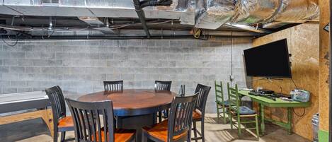 A conference room with a round table, six chairs, a television, and a workbench.