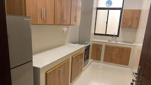 A compact kitchen with wooden cabinets, a built-in oven, and a refrigerator. - RED-33 - Gardenia (Salalah)