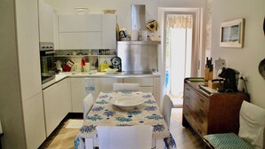 A compact kitchen with white cabinets, a stainless steel range hood, and a dining table set with a white tablecloth.