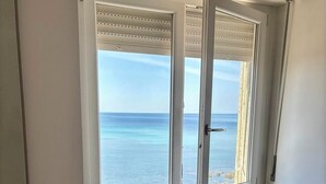 A corner room with a view of the sea through a window with shutters, a radiator, and a wooden chair.
