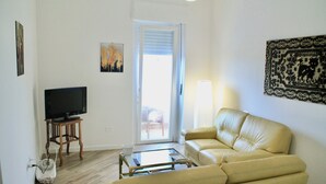 A living room with a sofa, a coffee table, a television, and a door leading to an outdoor area.