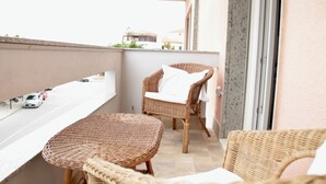 A balcony with wicker furniture, a white cushion, and a view of buildings in the background.