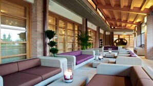 A modern lounge area with sofas and ottomans, large windows, and a wooden ceiling.