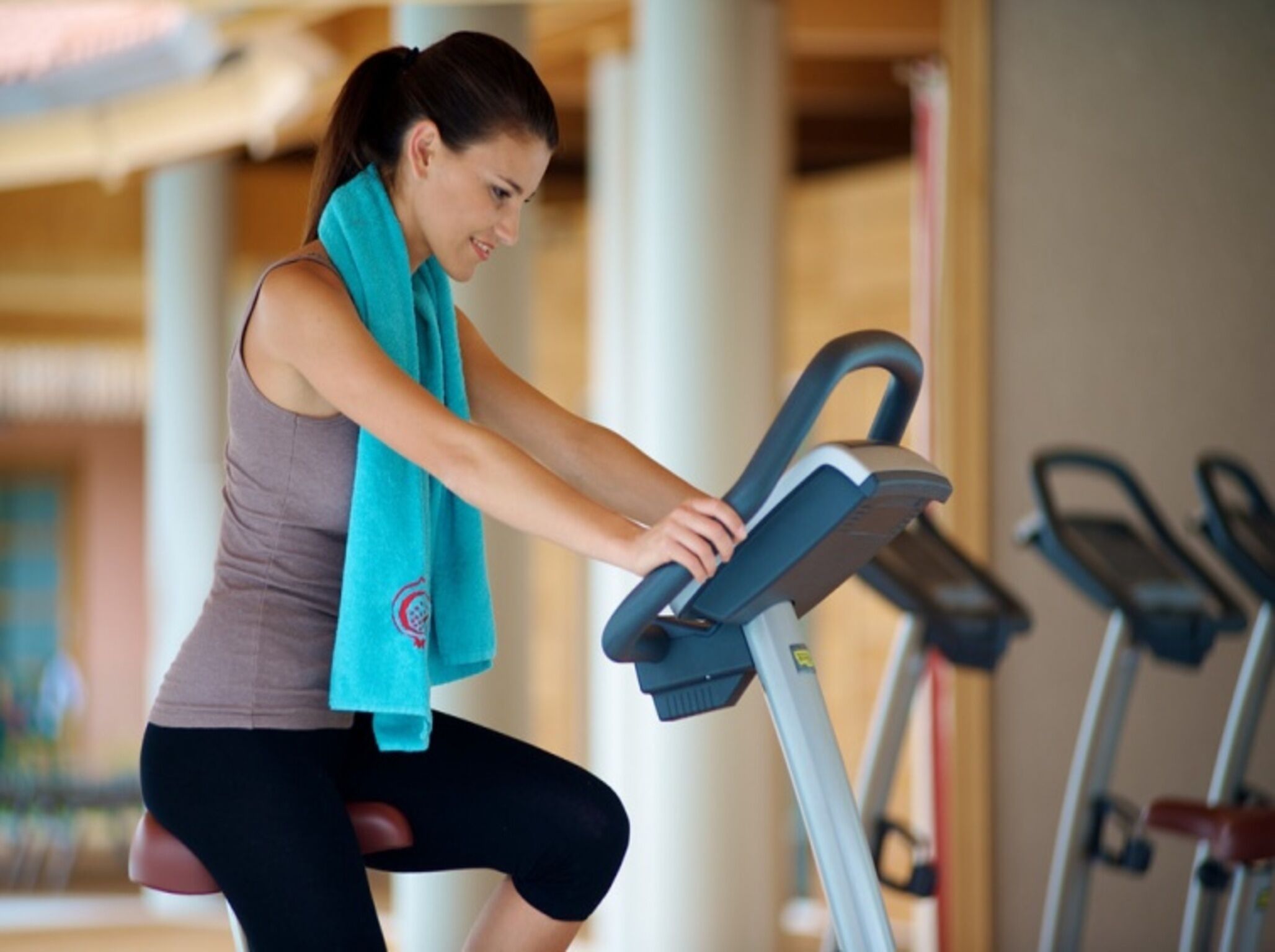 A person using a stationary bike in a gym with multiple bikes and a large pillar in the background.