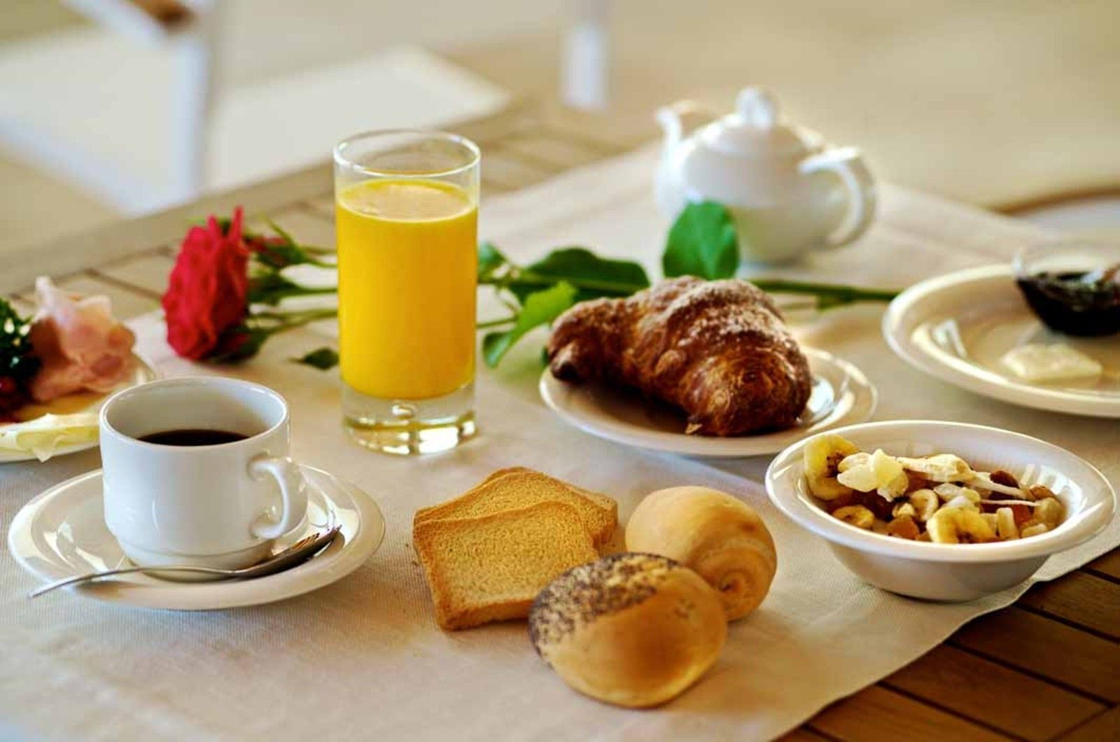 A breakfast setting with toast, croissants, a bowl of fruit, a cup of coffee, and a glass of orange juice on a table.