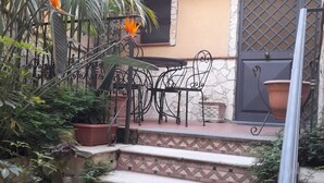 A staircase leading to a patio with a metal table and chairs, surrounded by potted plants and a stone wall.