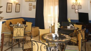 A well-lit living room with a chandelier, a painting on the ceiling, and a dining area with chairs and tables.