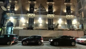 A building with multiple balconies and a sign indicating a hotel. There are several parked cars in front of the building.