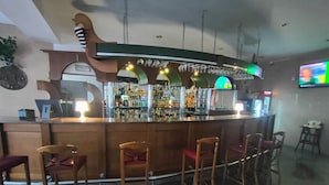 Un'area bar con un bancone in legno, diversi sgabelli e una varietà di bottiglie e bicchieri.
