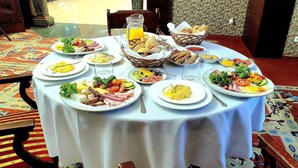 Un tavolo rotondo con diversi piatti di cibo per la colazione, una caraffa di succo d'arancia e un cestino di pane.
