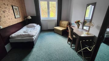 Quarto de hotel com uma cama, um sofá, uma escrivaninha com cadeira, um espelho e uma janela com cortinas.