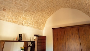 A room with a stone ceiling, wooden wardrobe, and a shelf with decorative items. - Olive Estate (Puglia)