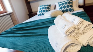 A neatly made bed with a teal bedspread, white pillows, and rolled towels. - Olive Estate (Puglia)