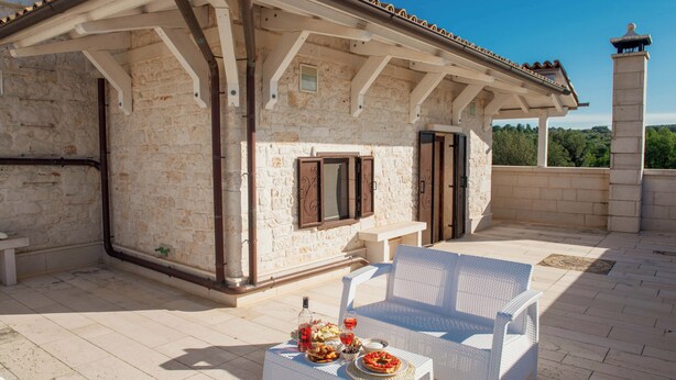 A covered outdoor seating area with stone walls, a white wicker sofa, and a table set with food and drinks. - Olive Estate (Puglia)