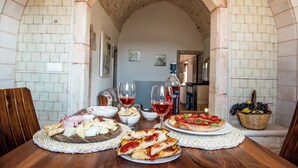 A dining table with various food items and wine glasses, set in a room with stone walls and an arched doorway. - Olive Estate (Puglia)