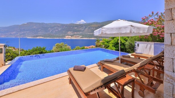 Una piscina amb vistes al mar, gandules i un parasol blanc.